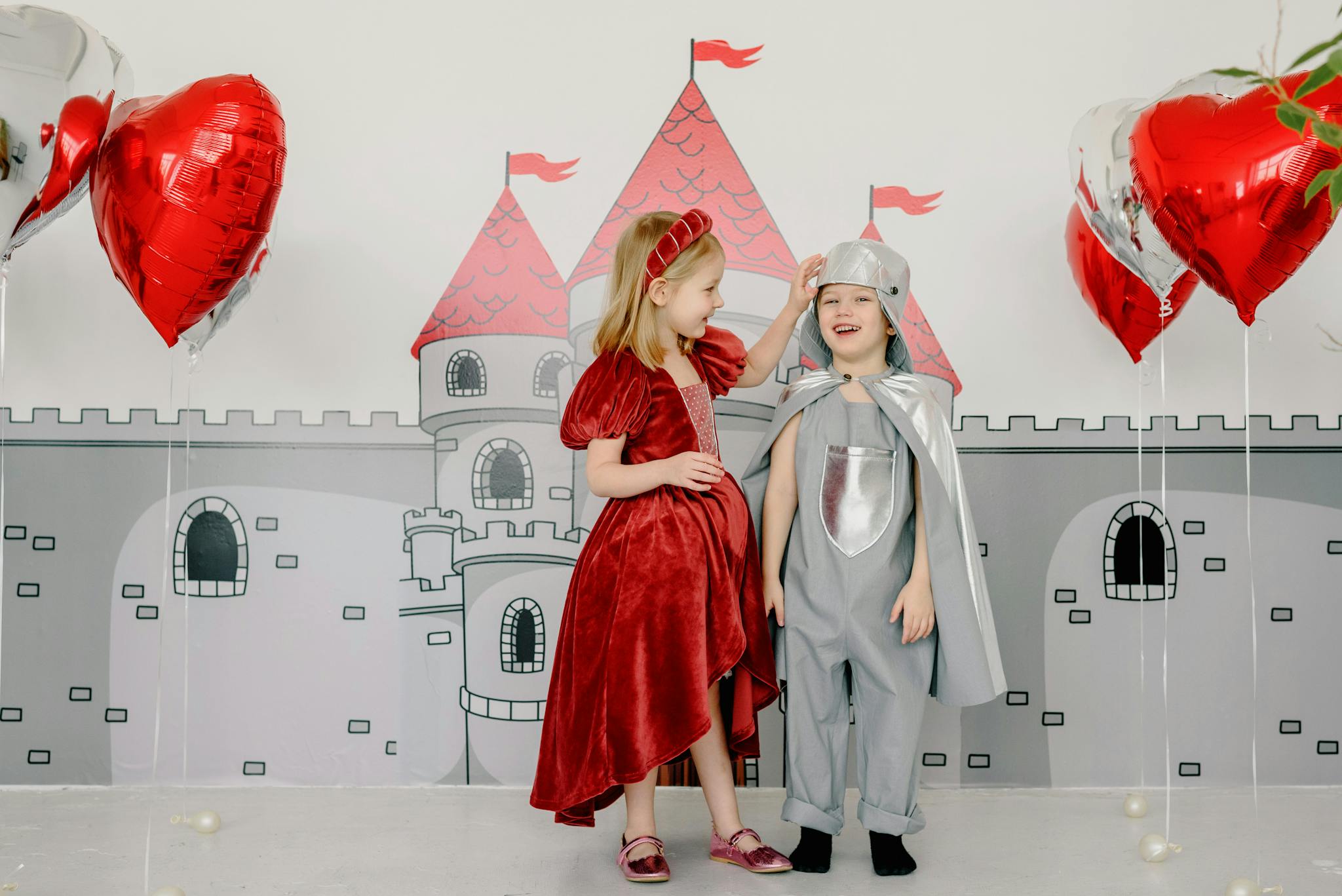 Kids dressed as a knight and princess with heart balloons and castle mural.